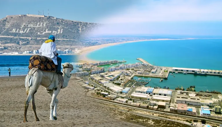 Agadir: A man rides a camel along the beach, with the ocean visible in the background under a clear sky.